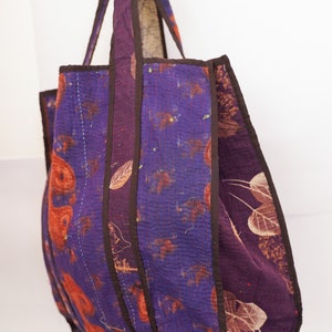 Puede incluir: Un bolso tote grande, morado y marr&oacute;n con un dise&ntilde;o de patchwork. El bolso tiene un fondo ancho y plano y dos asas largas.
