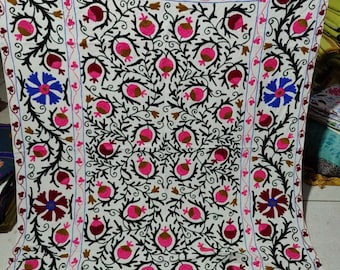 May include: A white cotton fabric with intricate embroidery featuring a floral design with pink, brown, and blue flowers. The embroidery is done in black thread and creates a detailed pattern.