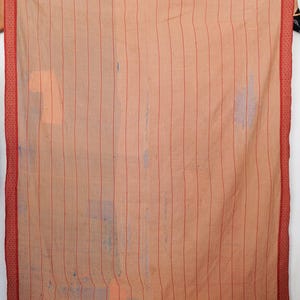 Puede incluir: Textil color melocotón con costuras verticales rojas y un borde rojo. El borde presenta un patrón de puntos. El textil parece ser una manta o colcha, con desgaste visible.