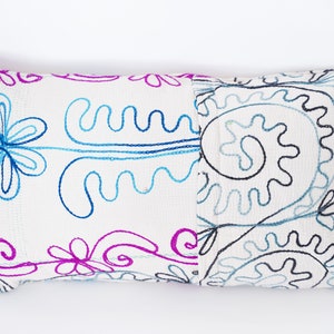 May include: White rectangular pillow with embroidered floral designs in blue, pink, and black.