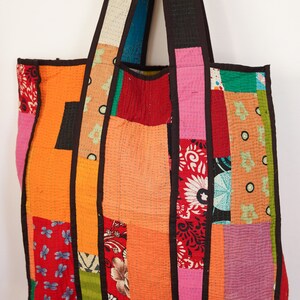May include: A patchwork tote bag with a variety of colorful fabrics, including red, orange, pink, green, and blue. The bag has two brown straps and is made of a quilted material.