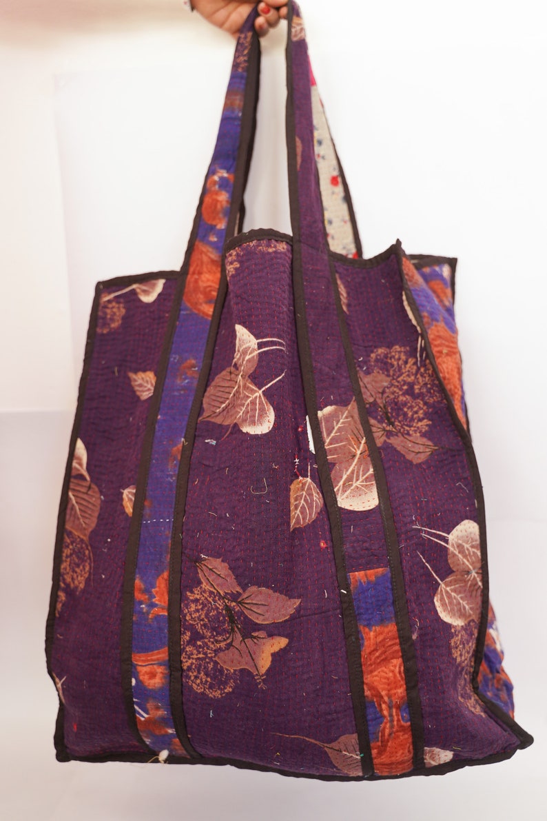 Puede incluir: Una gran bolsa de mano de color morado con correas marrones y estampado floral. La bolsa est&aacute; hecha de tela acolchada y tiene un dise&ntilde;o &uacute;nico de patchwork.