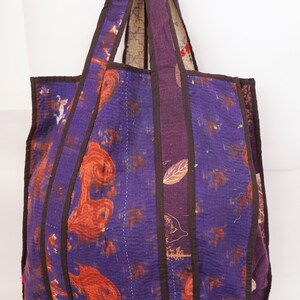Puede incluir: Una gran bolsa de mano de color morado con asas marrones. La bolsa est&aacute; hecha de tela de patchwork con una variedad de patrones y colores. La bolsa es perfecta para llevar comestibles, libros u otros art&iacute;culos.