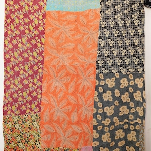 Pode incluir: Têxtil de patchwork com uma variedade de padrões florais e geométricos. A colcha apresenta secções de tecidos vermelhos, laranja, pretos e azuis. Os padrões incluem grandes desenhos de folhas, pequenas flores e um padrão de grade.