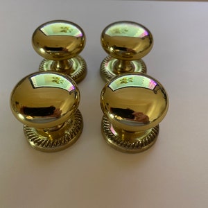 May include: Four polished, gold-coloured cabinet knobs with a spherical design. Each knob features a decorative, rope-style detail around the base. The knobs reflect the surroundings, adding a touch of elegance to any furniture.