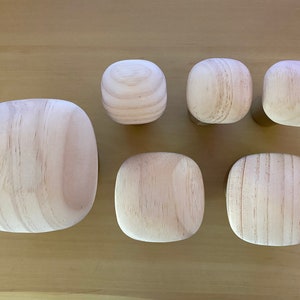 May include: A selection of unfinished wooden knobs and pulls in various shapes. The set includes rounded square and spherical designs, all with a natural wood grain finish. These are likely for furniture or cabinet hardware.