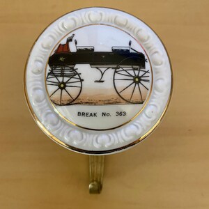 May include: A white ceramic wall hook featuring a gold-edged design and a carriage illustration. The carriage is black with red details, and the text "BREAK No. 363" is printed below the image.