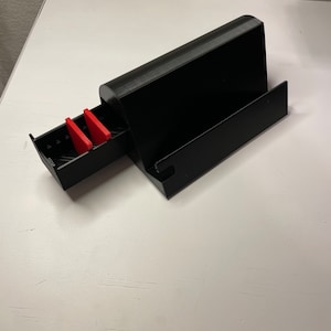 May include: A black plastic storage box with a drawer that slides out. The drawer has two red plastic dividers inside.
