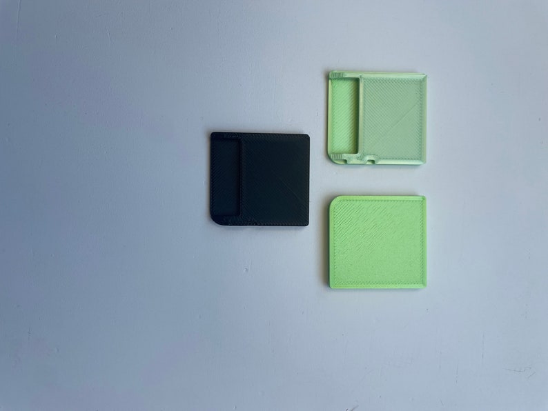 May include: Three 3D printed plastic cases, two are light green and one is black. The cases have a rectangular shape with a slot in the middle.