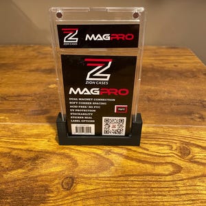 May include: A clear plastic MAGPRO card holder with a black base. The holder features the text "ZION CASES" and "MAGPRO" in red and white. Additional text includes "DUAL MAGNET CONNECTION" and "75PT".