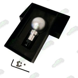 以下が含まれることがあります： 黒い箱に入った、球状のトップが付いたシルバーのシフトノブ。ノブは円筒形のベースで、小さな金属部品と六角レンチが付属しています。 パッケージはミニマルでモダンです。