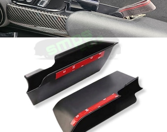 May include: Two black plastic storage containers with adhesive backing. The containers are designed to fit in the door panel of a car.
