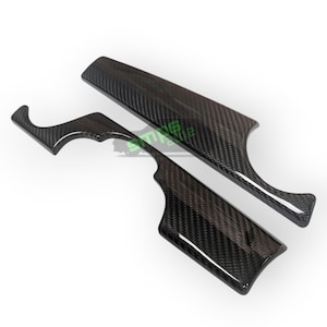 Könnte beinhalten: Zwei Carbonfaser-Zierleisten für den Innenraum eines Autos. Die Teile sind schwarz mit einem gewebten Muster und einer glänzenden Oberfläche. Ein Teil ist lang und rechteckig, das andere ist gebogen und hat eine hakenartige Form.