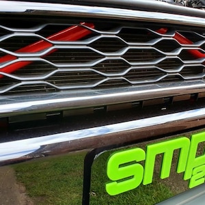 Puede incluir: Un coche negro con una parrilla roja y negra y una placa verde que dice "SMPS 2012".