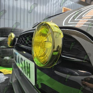 May include: A close-up of a black car with a yellow round fog light. The car has a number plate that reads "014 SAM".