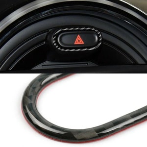 Może przedstawiać: Zbliżenie na czarny pierścień ozdobny wnętrza samochodu z włókna węglowego z czerwonym przyciskiem ostrzegawczym.