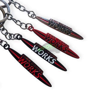 May include: Keyrings with a metallic finish. Each keyring features a red, black, and silver design with the text "JOHN COOPER WORKS". The keyrings are attached to a silver chain.