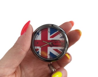 May include: A silver car clock with a Union Jack design and a red Mini Cooper silhouette. The clock face has black numbers and hands.