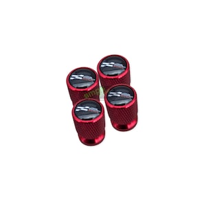May include: Four red tyre valve stem caps with a black and white emblem on top. The caps are cylindrical with a textured surface. The emblem features a checkered flag design.