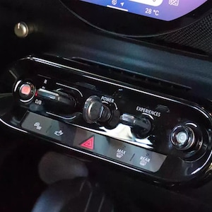 Op de afbeelding: Close-up van een dashboard van een auto met een rij knoppen. De knoppen zijn gelabeld "D/S", "Power", "Experiences", "Max" en "Rear".