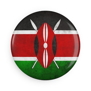 Puede incluir: Un botón redondo con el diseño de la bandera de Kenia. El botón tiene un acabado brillante y un aspecto envejecido. El diseño de la bandera incluye franjas horizontales negras, rojas y verdes, con un escudo y lanzas cruzadas en el centro.