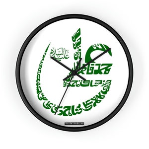 Könnte beinhalten: Runde Wanduhr mit schwarzem Rahmen und weißem Zifferblatt. Das Zifferblatt zeigt grüne arabische Kalligraphie. Die Zeiger der Uhr sind schwarz. Der Text "HaydarMaula.com" befindet sich am unteren Rand des Zifferblatts.