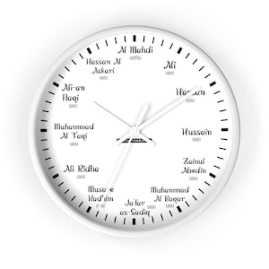 Könnte beinhalten: Weiße Wanduhr mit schwarzen Ziffern und Zeigern. Das Zifferblatt zeigt Namen in schwarzer Schrift, darunter "Al Mahdi" und "Hassan Al Askari". Die Uhr hat ein schlichtes, modernes Design.