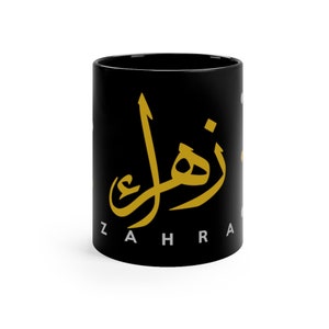 May include: Black ceramic mug with gold Arabic calligraphy and the English word "ZAHRA" printed on the side. The mug is cylindrical and has a glossy finish, suitable for hot or cold beverages.
