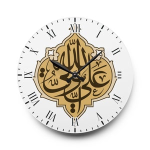 Könnte beinhalten: Weiße Wanduhr mit schwarzen römischen Ziffern und Zeigern. Das Zifferblatt zeigt in der Mitte ein gold-braunes arabisches Kalligraphie-Design. Die Zeiger zeigen auf etwa 10:50 Uhr.