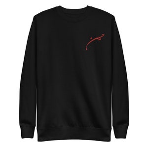 Könnte beinhalten: Schwarzes Sweatshirt mit langen Ärmeln. Auf der linken Brustseite befindet sich ein roter Schriftzug. Der Schriftzug scheint in einer Fremdsprache verfasst zu sein. Das Sweatshirt ist aus weichem Material.