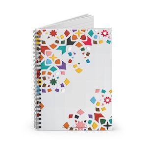 May include: A spiral-bound notebook with a white cover, adorned with a vibrant geometric pattern. The design showcases a variety of shapes and colours, including red, blue, yellow, and green. The notebook's pages are lined, and the website address www.hamdarmaula.com is printed.