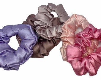 May include: Set of four satin scrunchies in shades of purple, pink, and brown. The scrunchies are made of soft, silky fabric and are perfect for holding hair in place.
