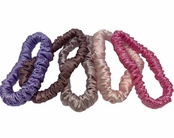 May include: Set of five hair scrunchies in shades of purple, brown, pink, and light pink. The scrunchies are made of a soft, silky material.