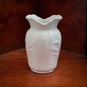 May include: A white ceramic jug featuring a scalloped rim and embossed wheat stalk patterns on the exterior. The vessel has a rounded body with a smooth, glossy finish and a wide opening, showcasing a clean, solid colour design throughout.