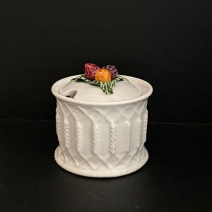 May include: White ceramic sugar bowl with a lid decorated with colourful fruit. The bowl has a textured diamond pattern and a small spoon rest. A charming addition to any kitchen.