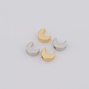 Peut inclure: Quatre perles en métal en forme de croissant de lune, deux dorées et deux argentées, sur un fond blanc.