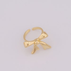 May include: A gold-coloured ring featuring a bow design. The bow is crafted from metal and has a smooth, shiny finish.