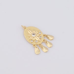 May include: Gold-colored pendant with an oval shape, featuring a starburst design with clear crystal accents. The pendant has a textured surface and includes dangling teardrop-shaped charms. A jewelry component.