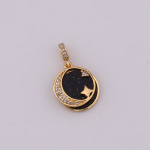 May include: Gold pendant charm featuring a black crescent moon with a small gold star inside. The moon is surrounded by a circle of small clear rhinestones.