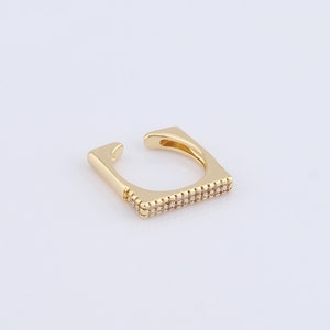 Puede incluir: Un pendiente de aro dorado con forma cuadrada y una fila de pequeñas piedras transparentes alrededor del borde.