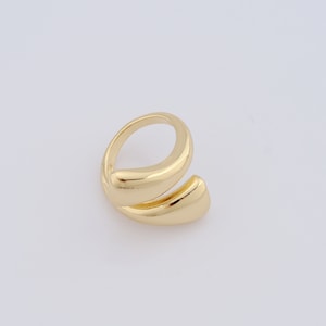 Könnte beinhalten: Ein goldfarbener Ring mit einem einzigartigen, gedrehten Design. Der Ring ist aus glattem, poliertem Metall gefertigt und hat eine schlichte, moderne Ästhetik.