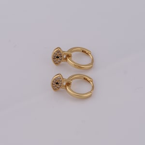 May include: A pair of gold hoop earrings with a small evil eye charm. The charm is decorated with clear cubic zirconia stones and a black centre.