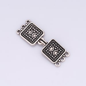 May include: Silver-toned metal connector with a square design and intricate details. The connector has four loops on each side for attaching jewelry or other crafts.