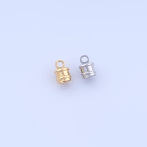 May include: Two small cylindrical cord ends with a top loop for attachment. One cord end is finished in a polished gold tone, and the other is finished in a polished silver tone. Both pieces feature a smooth, rounded body with a raised band detail.