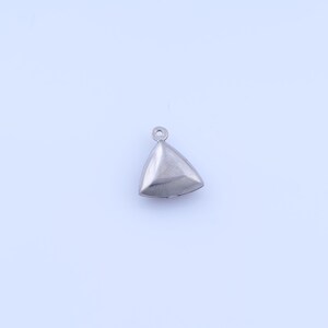 Puede incluir: Un pequeño colgante triangular plateado con un lazo en la parte superior. El colgante tiene una superficie lisa y reflectante y una forma tridimensional. La pieza de joyería es probablemente para collares o pulseras.