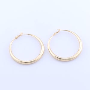 May include: A pair of gold hoop earrings. The earrings are large and have a smooth, rounded finish.