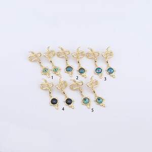 May include: Gold-toned earrings featuring a snake design with an evil eye pendant. The pendants have blue and white details. The earrings are displayed on a white surface.
