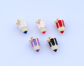 Può includere: Cinque ciondoli a forma di matita colorata con dettagli color oro. Ogni ciondolo presenta una diversa combinazione di colori: bianco e blu, bianco e rosa, rosso, viola e nero. I ciondoli sono posti su uno sfondo chiaro.