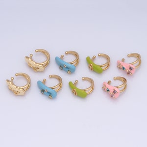 May include: Eight gold-tone rings with colourful enamel and rhinestones. The rings are in different shapes, including a cloud, a heart, and a rectangle. The rings are all double-banded.