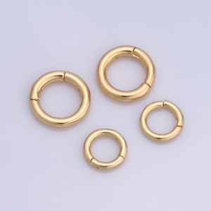 May include: Four gold-colored metal jump rings of different sizes. The rings are open and have a smooth finish.